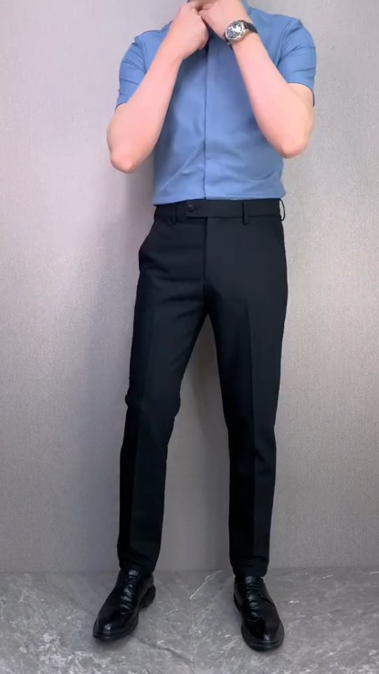 Man wearing a light blue short sleeve shirt tucked into black tailored trousers with black dress shoes and a watch