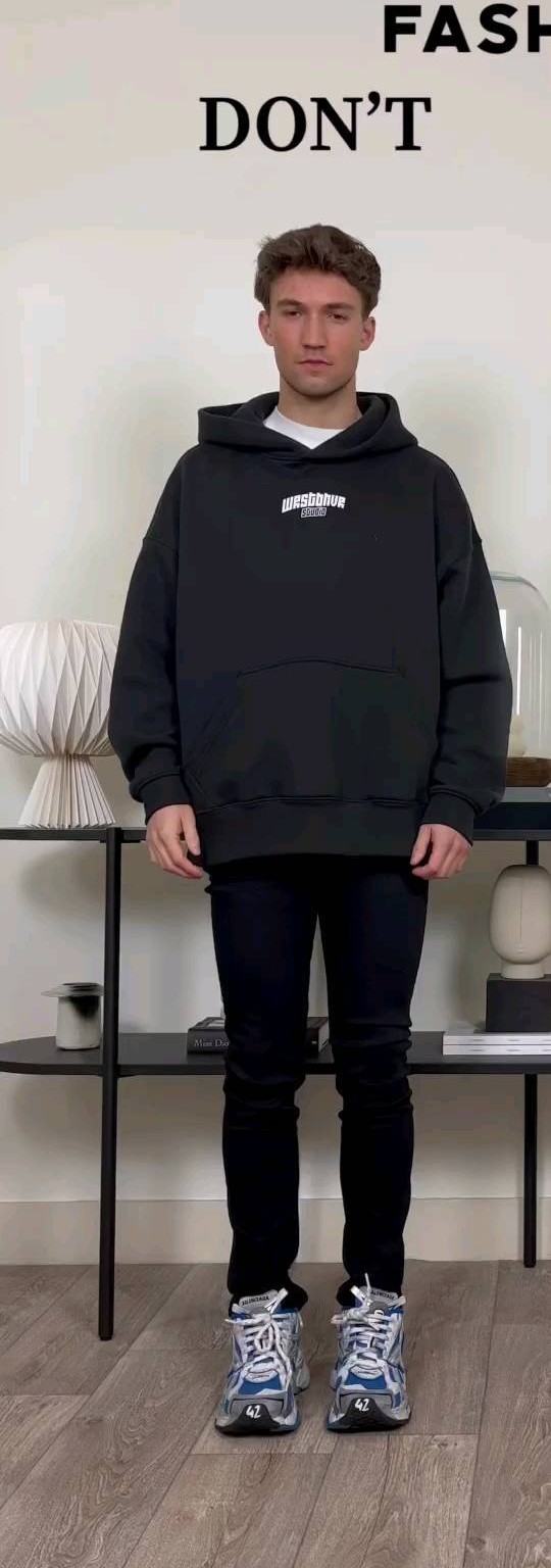 Man in a black oversized hoodie with tight skinny jeans and chunky sneakers, showing a top-heavy silhouette