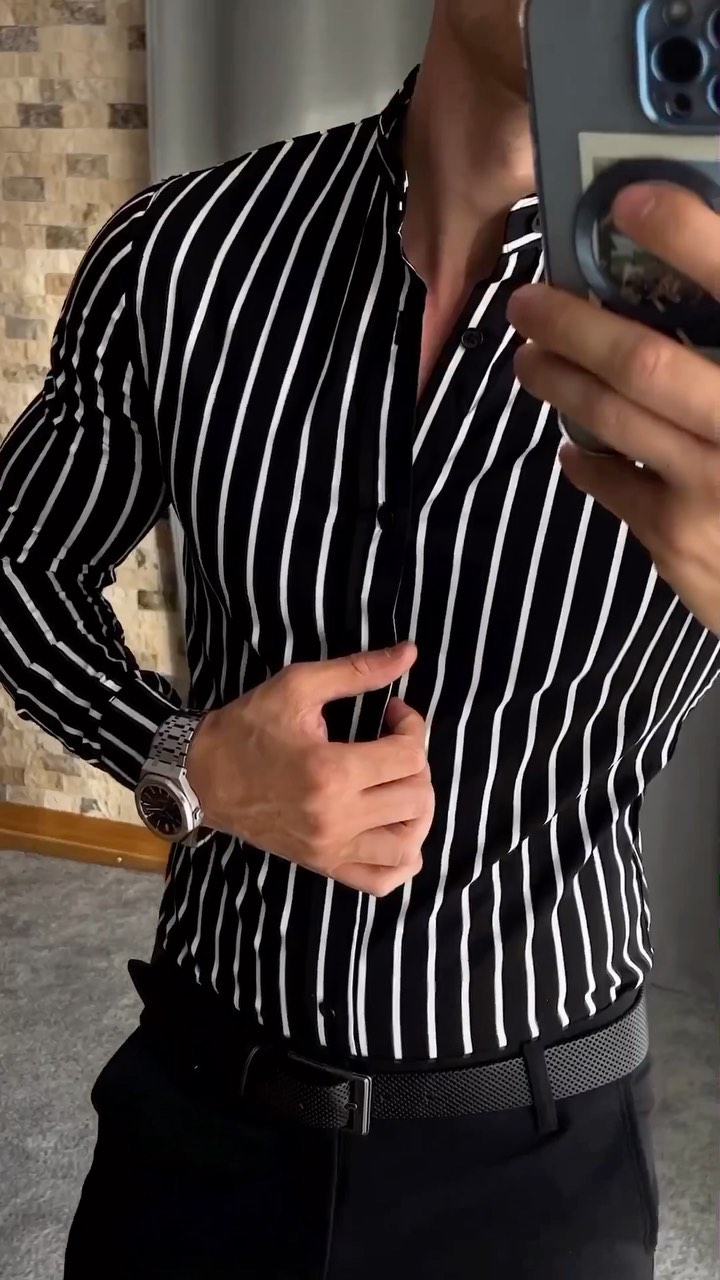Man wearing a black and white vertical-striped band collar shirt tucked into dark trousers with a black belt