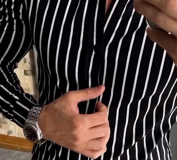 Torso view of a vertically striped band collar shirt with buttoned cuff and restrained metal watch
