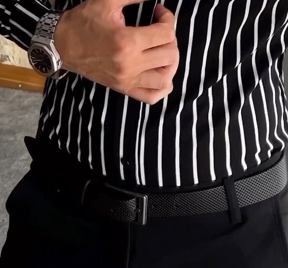 Close view of a striped shirt tucked into dark trousers with a textured black belt and simple metal buckle