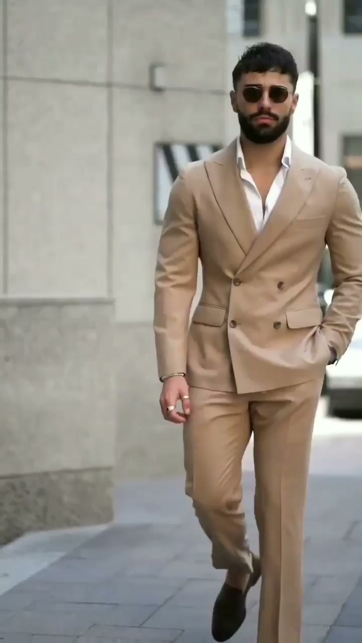 Man walking outdoors in a tan double-breasted suit, open white collared shirt and dark loafers