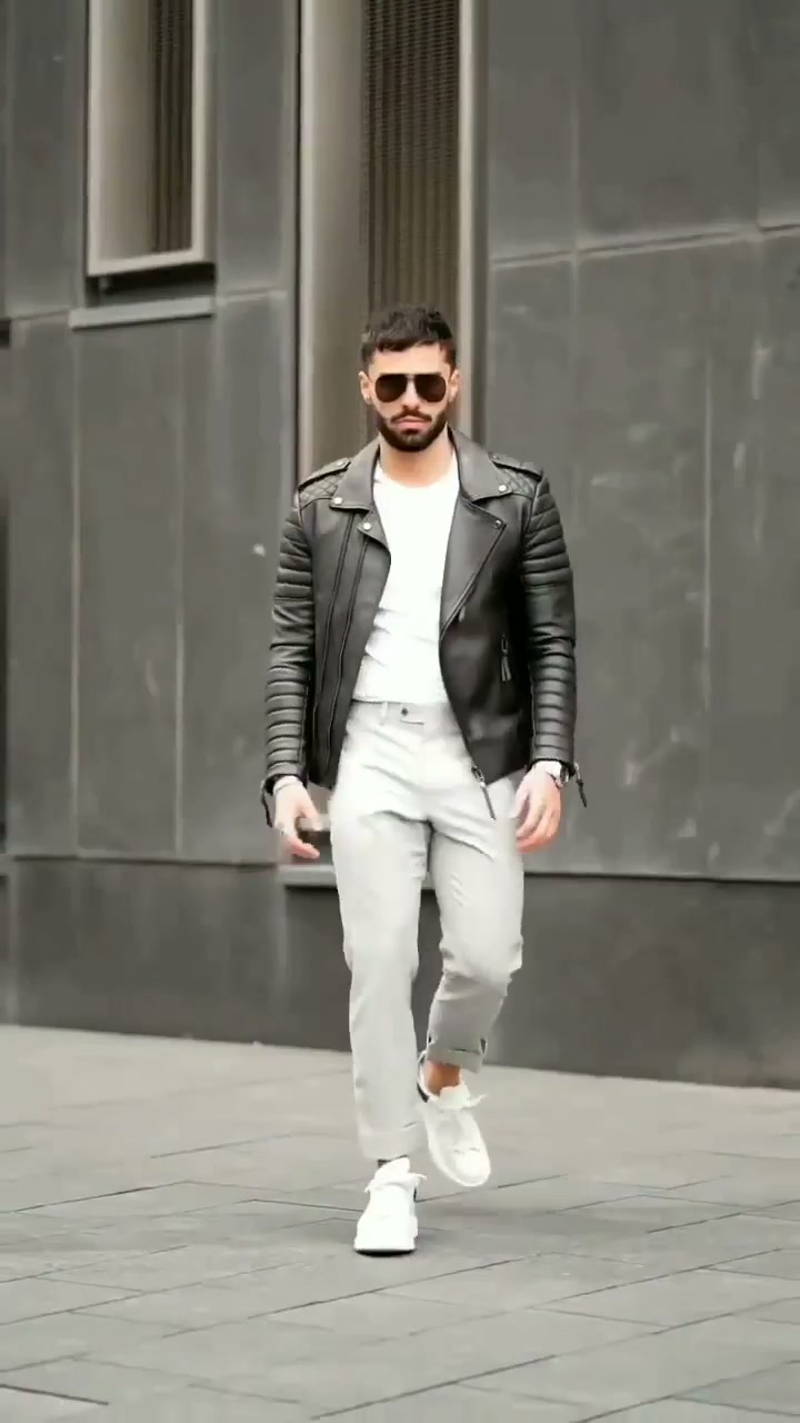 Man in a dark jacket, white T-shirt, light grey cropped trousers and white sneakers outdoors