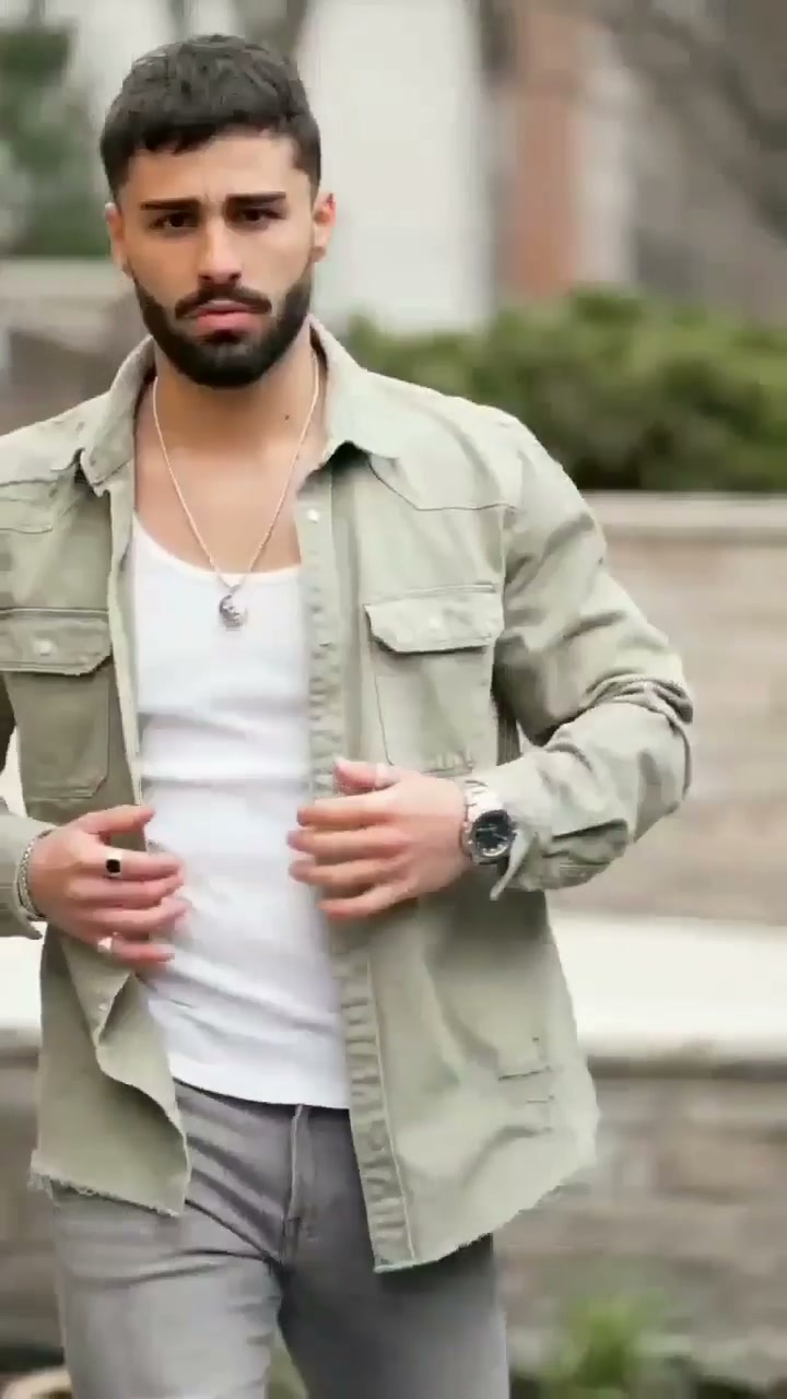 Man adjusting a sage-green overshirt over a white base with light casual trousers