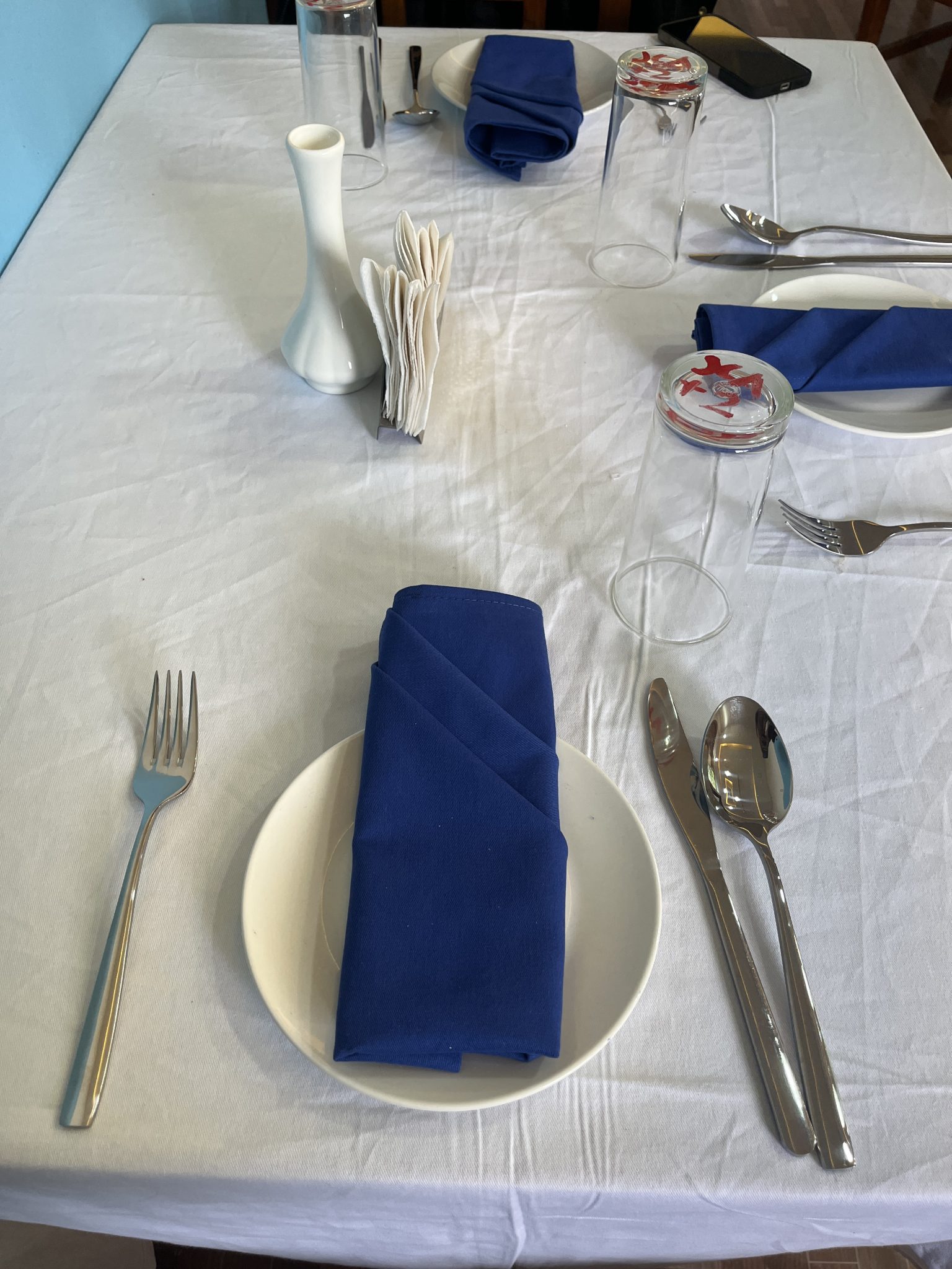 A complete restaurant table setting with white linen, blue napkins, cutlery and glassware