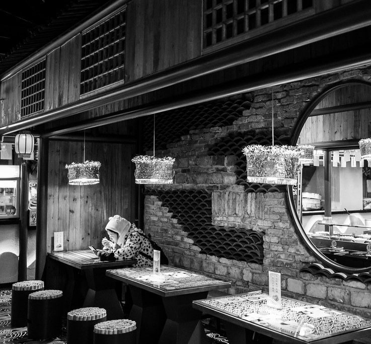 Wider restaurant view showing tables, stools, menus and one patron with a lit device