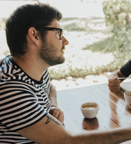 A man in a striped shirt using an open-hand gesture during a conversation at a table