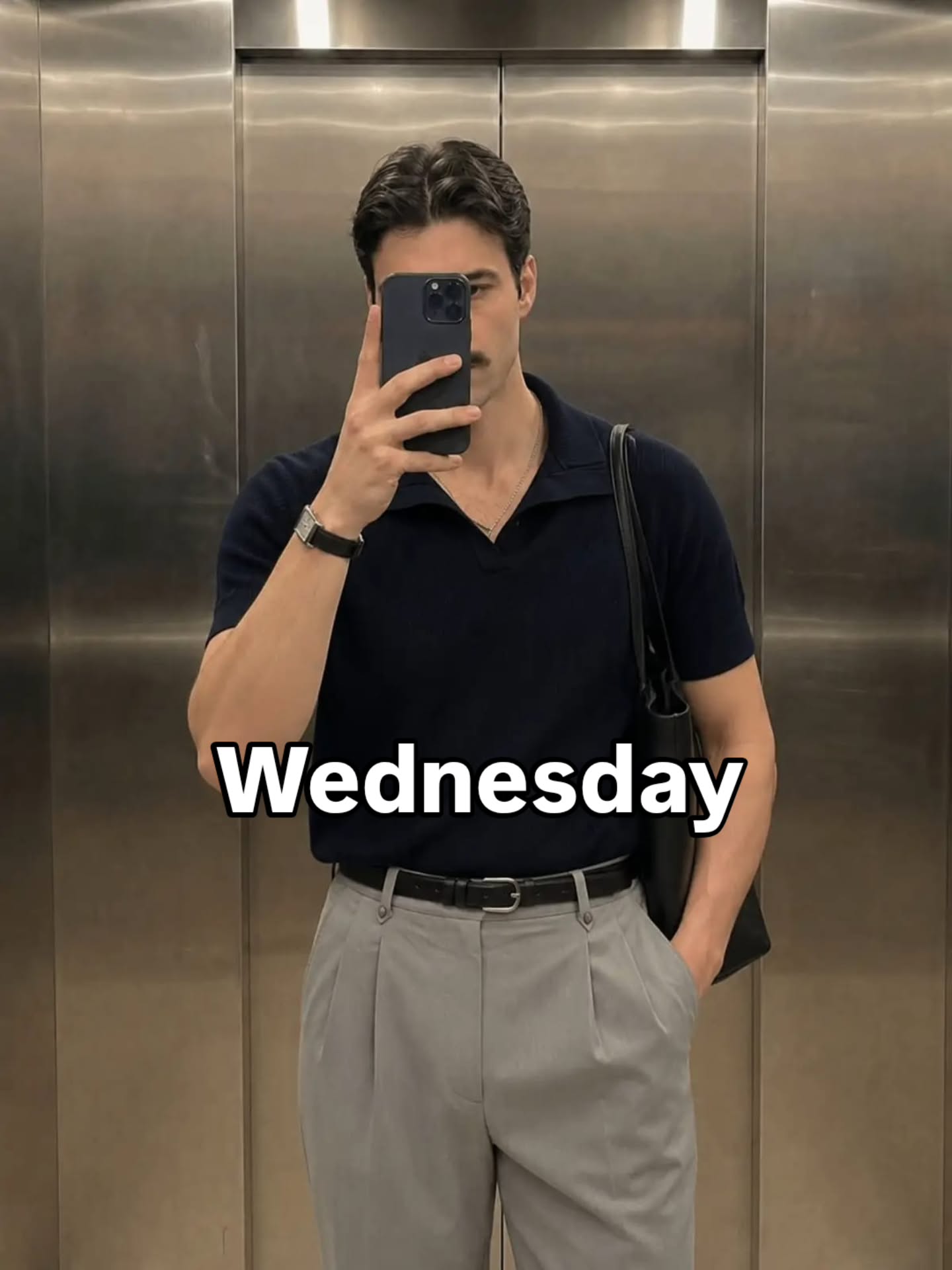 Dark navy short-sleeve knit polo tucked into light grey high-waisted pleated trousers with a black belt and shoulder bag strap