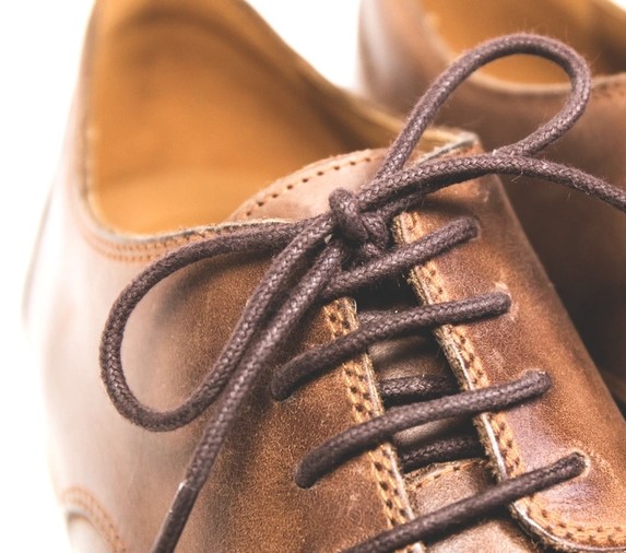 Close-up of the lacing and eyestay on a tan leather shoe, showing neat double-row stitching along the facing