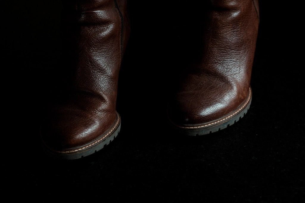 Dark brown leather boots worn on the feet against a dark background, showing natural flex creases across the toe and a visible welt line above the sole