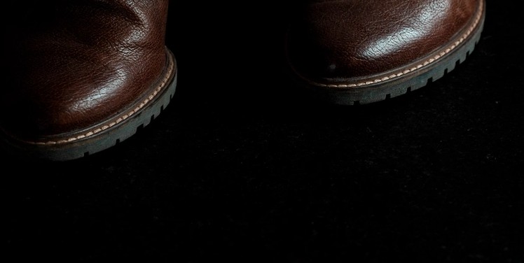 Close-up of the toe and welt area of brown leather boots, showing the contrast welt stitching line above a lugged rubber sole edge
