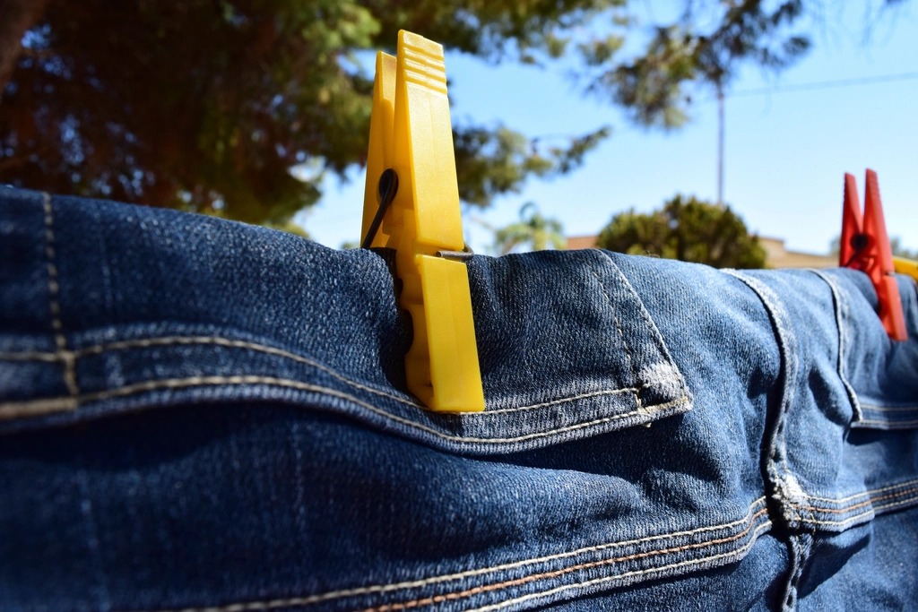 Two pairs of jeans air-drying on an outdoor clothesline, hung by the waistband with clothespins