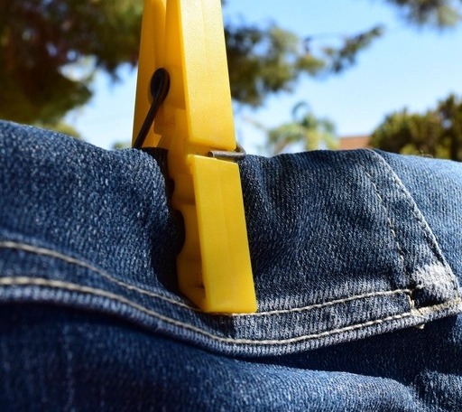 Close-up of clothespin placement at the back yoke of hanging jeans, with straight legs and clean hems